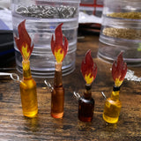 A close image of four tiny bottles with tiny flames coming out of them. Two lager bottles - one light amber and one darker amber, and two whiskey bottles - one very dark bottle and one light amber.