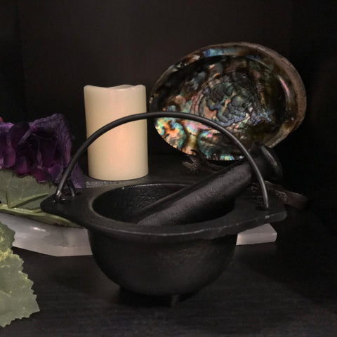 6Witch3 Cast Iron Cauldron with Pestle - Shown with the pestle resting in the bowl in front of a selenite incense burner, a candle, and an abalone shell.