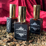 6Witch3 Agua Florida Florida Water - three square glass bottles with gold tops laying on a bed of brown herbs in front of a backdrop of red velvet