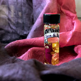 6Witch3 Scent Oil Sara La Kali - a 2 dram bottle of oil stands on a purple and pink pile of silk scarf. The oil bottle has a bit of rose petal and 24k gold leaf in the bottle along with the slightly golden oil. 