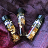 6Witch3 Scent Oil Sara La Kali - three 2 dram bottles of oil lay on a purple and pink pile of silk scarf. The oil bottles have a bit of rose petal and 24k gold leaf in the bottles along with the slightly golden oil.