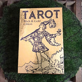 6Witch3 Tarot Black & Gold Edition - The cover of the box shown on a circle of green moss resting on a brown wooden background.