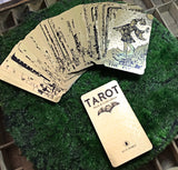 6Witch3 Tarot Black & Gold Edition - The gilded cards are fanned out on a bed of green moss on top of a wooden background.