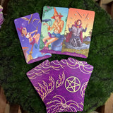 6Witch3 Teen Witch Tarot - A spread of cards and a small pile of facedown cards lay on a circle of green moss placed on a wood background.