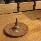 6Witch3 Dragon's Blood Incense Cones by Satya - a single brown cone sits on top of a cone burner tile that is balanced somewhat precariously on a wood stick incense ash catcher that is resting on a plank of wood next to three wooden boxes full of herbs in glass quart jars. This may be the most brown photo on the website.